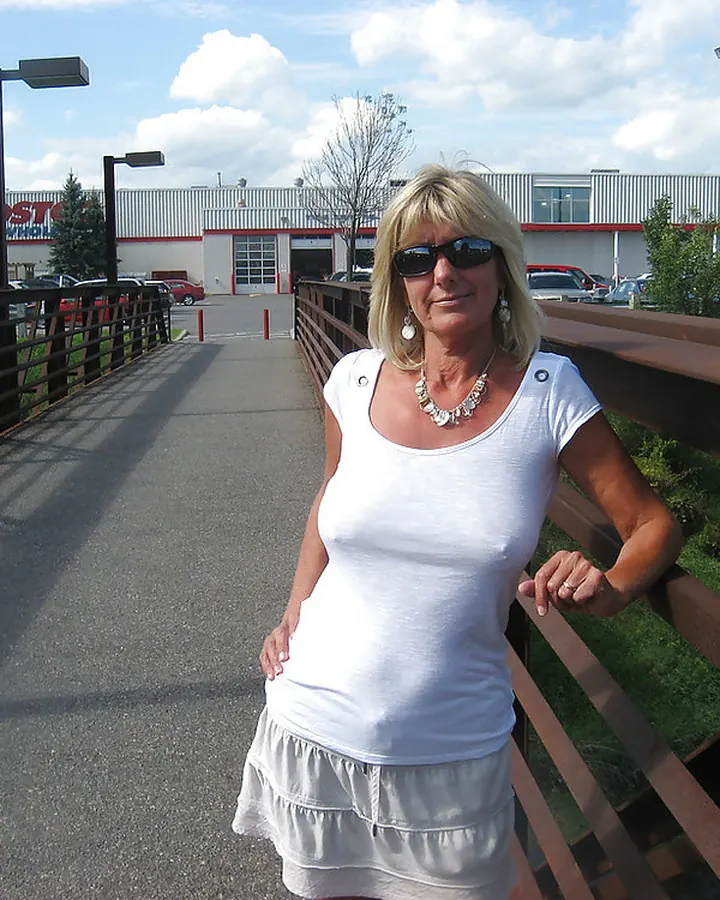 Femme blonde, portant une robe rouge, posant dehors, mains sur les hanches, souriante.